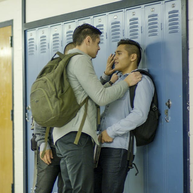 Two students in a confrontation by lockers in a school hallway.