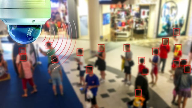 An AI-powered security camera analyzing a crowd in a public space, with red bounding boxes highlighting detected faces.
