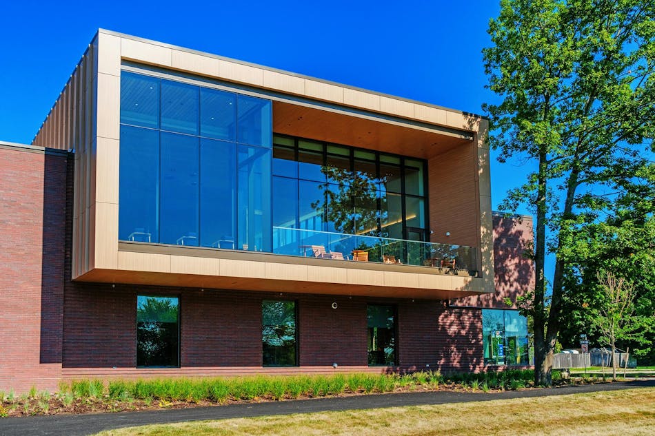 A modern brick and wood civic building with a cantilevered upper floor and glass curtain wall overlooking a terrace.